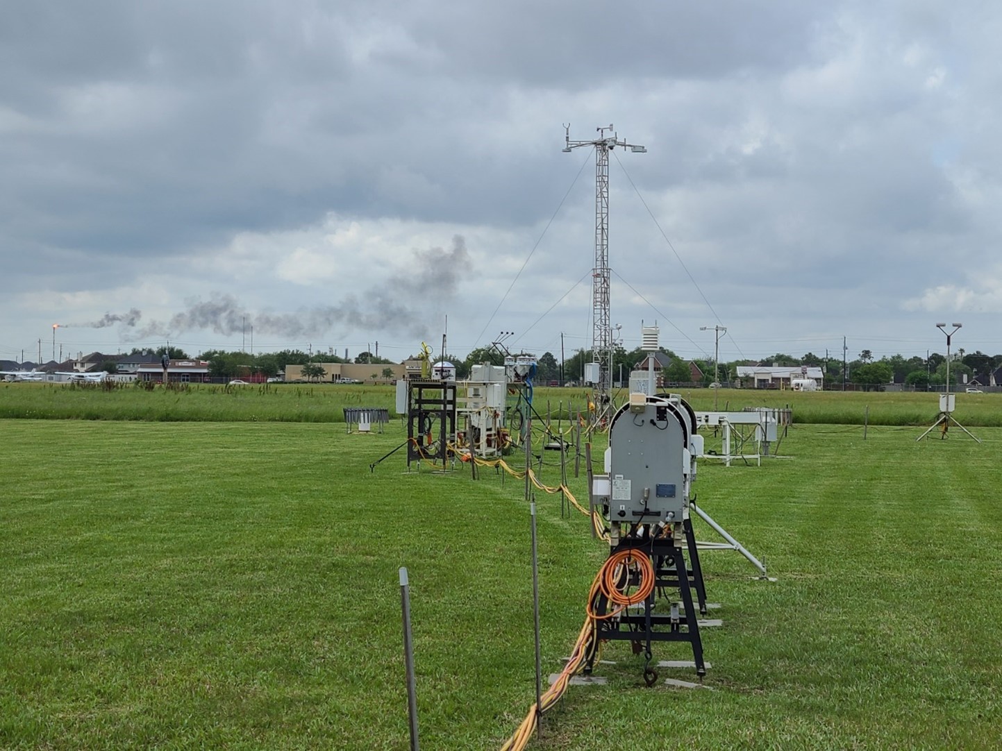 A plume rises from a chemical plant beyond a field of ARM instruments in La Porte. Photo is by Mark Spychala, Hamelmann Communications.