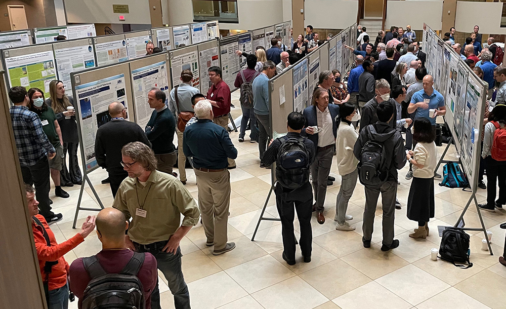 Matthew Shupe, standing toward the front of the atrium with his name tag visible, talks with colleagues during a poster session at the ARM/ASR joint meeting. Shupe co-coordinated the Multidisciplinary Drifting Observatory for the Study of Arctic Climate (MOSAiC) expedition in 2019 and 2020.